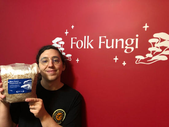 A man holds up a mushroom kit in front of red wall with a