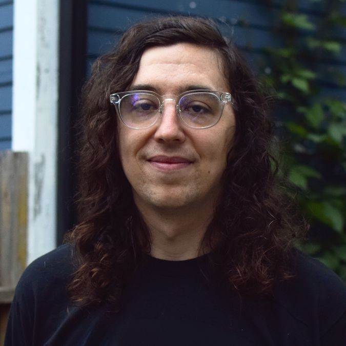 A man with long hair and clear glasses looks straight ahead.