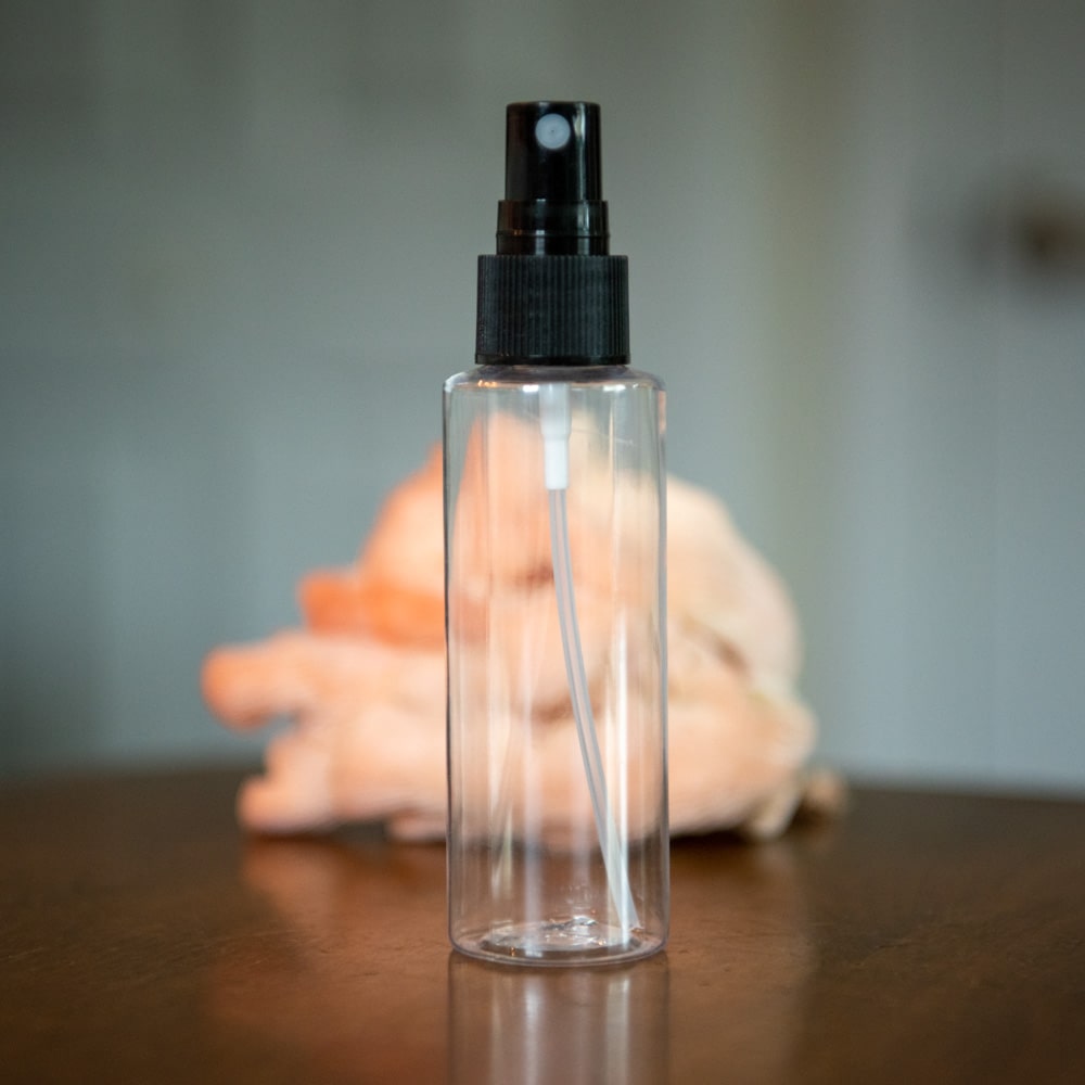 A spray bottle in front of some pink oyster mushrooms.